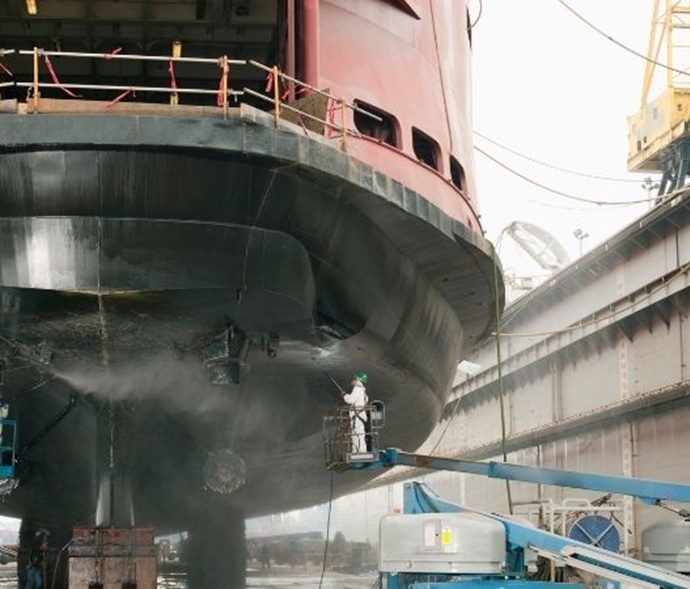 shipyard workers sandblasting a ship