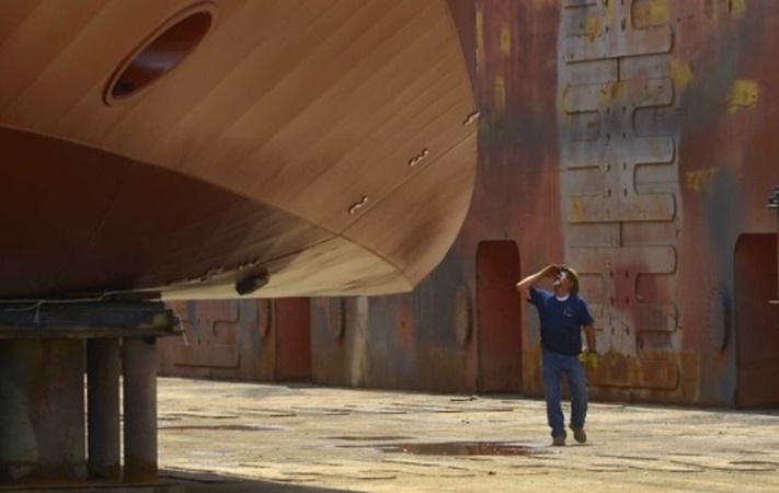 man walking in a dry dock looking up at a ship
