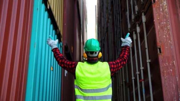 person in ppe with arms raised at cargo containers
