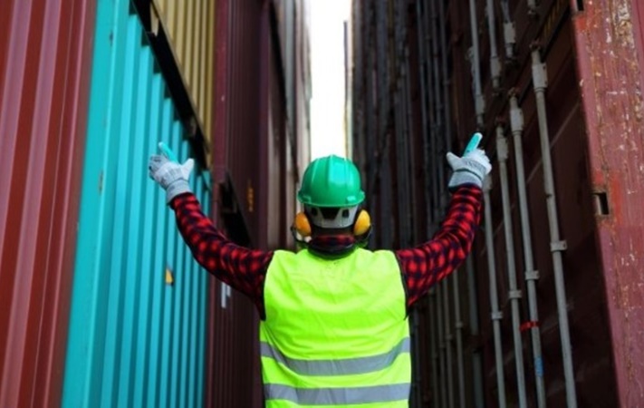person in ppe with arms raised at cargo containers