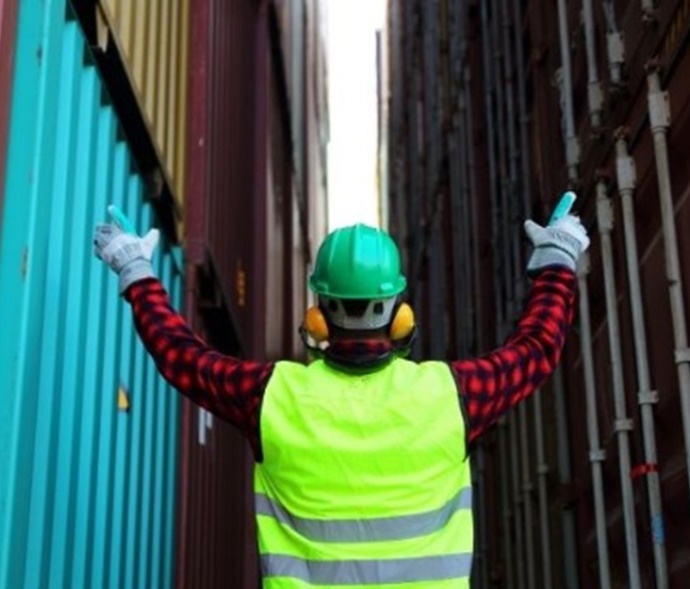 person in ppe with arms raised at cargo containers